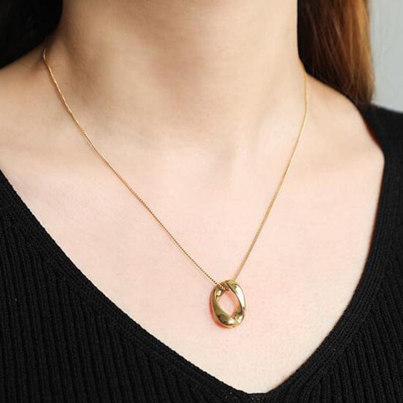 Bold minimalist twisted oval gold pendant necklace on model, showcasing glossy finish and unique design.