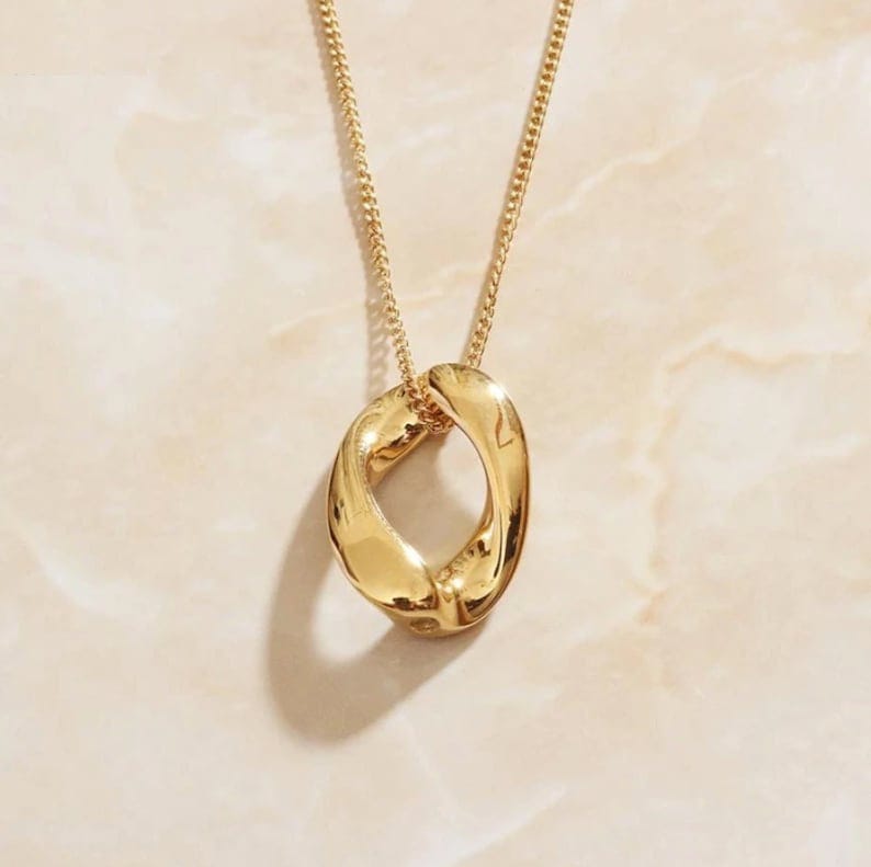 Bold minimalist twisted oval gold pendant necklace on a delicate chain, showcasing a glossy finish and unique sculpted design.